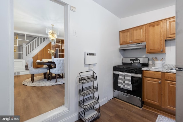 kitchen with stainless steel gas range oven, light stone countertops, dark hardwood / wood-style flooring, and an inviting chandelier