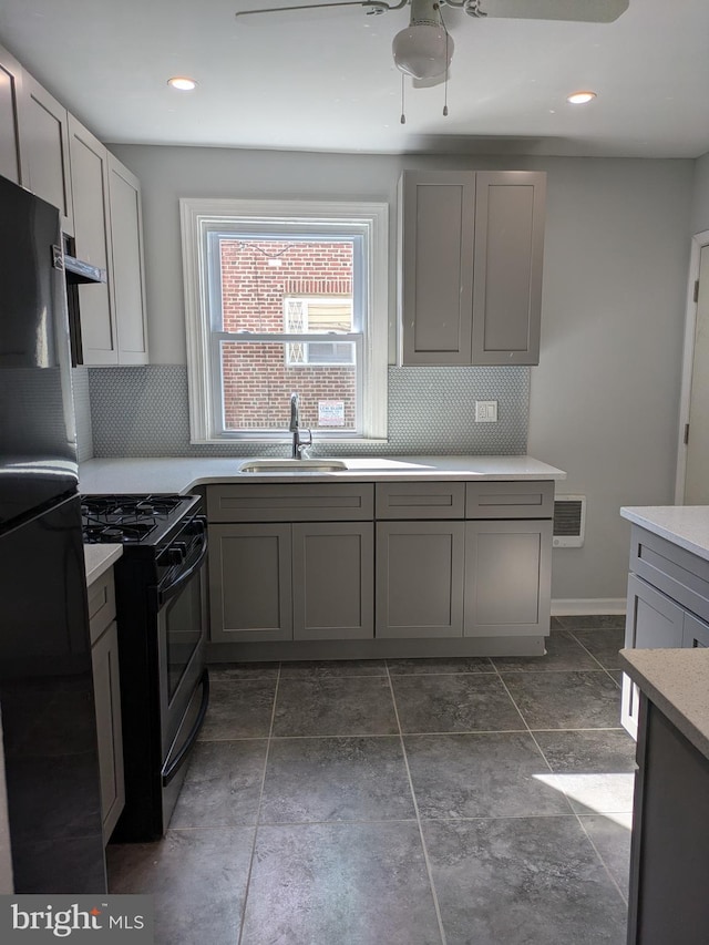 kitchen featuring gray cabinetry, gas stove, black fridge, and sink