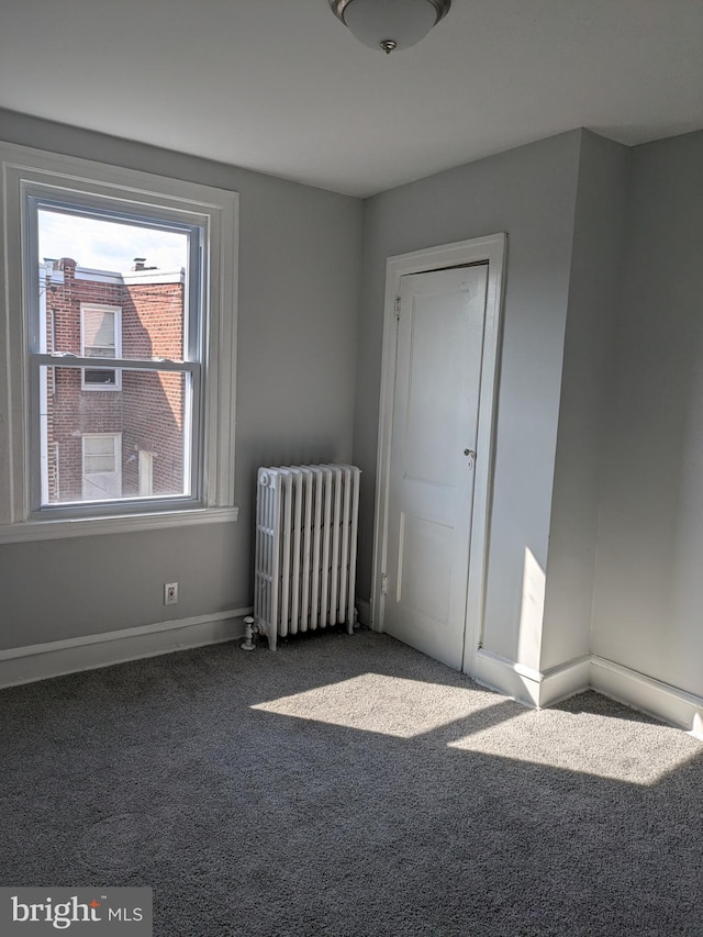 empty room with radiator heating unit and dark colored carpet