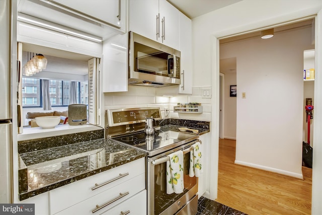 kitchen with dark stone counters, light hardwood / wood-style flooring, appliances with stainless steel finishes, tasteful backsplash, and white cabinetry