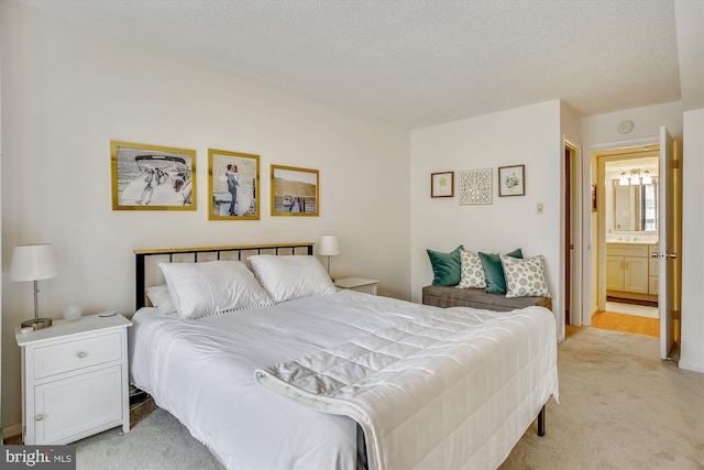 bedroom featuring a textured ceiling, light colored carpet, and ensuite bath