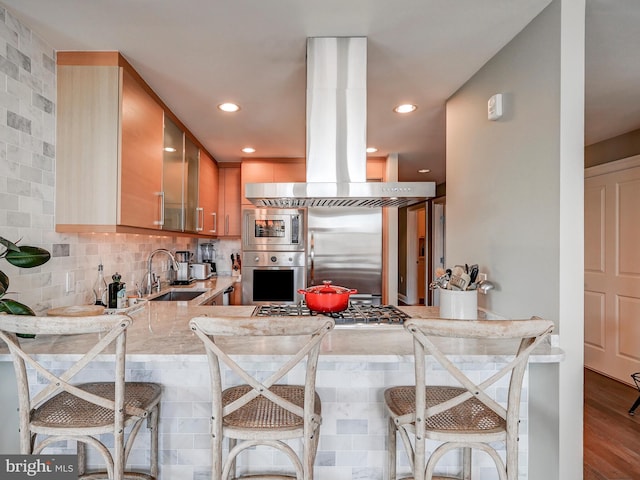 kitchen with kitchen peninsula, a kitchen bar, tasteful backsplash, sink, and built in appliances