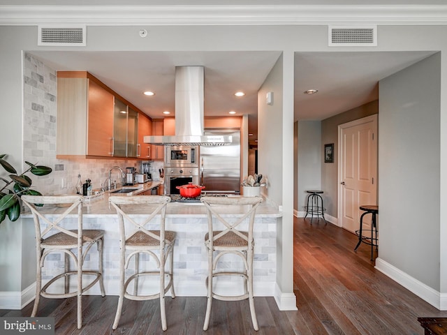 kitchen with backsplash, sink, built in appliances, a kitchen bar, and kitchen peninsula