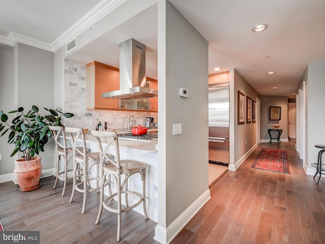 kitchen with ventilation hood, backsplash, kitchen peninsula, light hardwood / wood-style floors, and stainless steel built in fridge