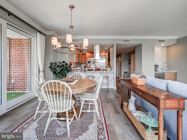 dining area with hardwood / wood-style flooring, ornamental molding, and a notable chandelier