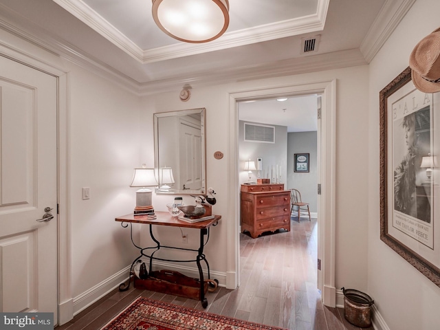 corridor with a raised ceiling, wood-type flooring, and ornamental molding