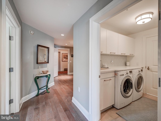 laundry area with washing machine and clothes dryer, light hardwood / wood-style flooring, and cabinets