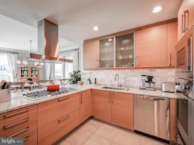 kitchen with appliances with stainless steel finishes, light stone counters, island range hood, sink, and light tile patterned flooring