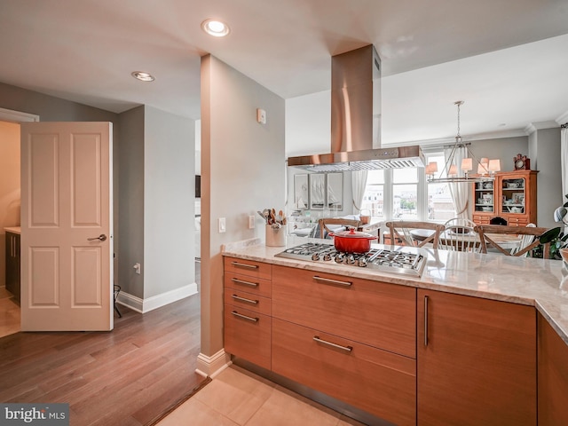 kitchen with a notable chandelier, stainless steel gas stovetop, light stone counters, and island exhaust hood