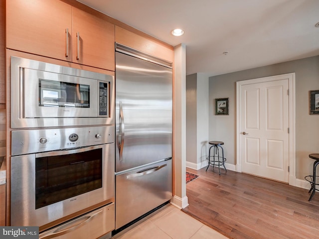 kitchen featuring light wood-type flooring, light brown cabinetry, and built in appliances