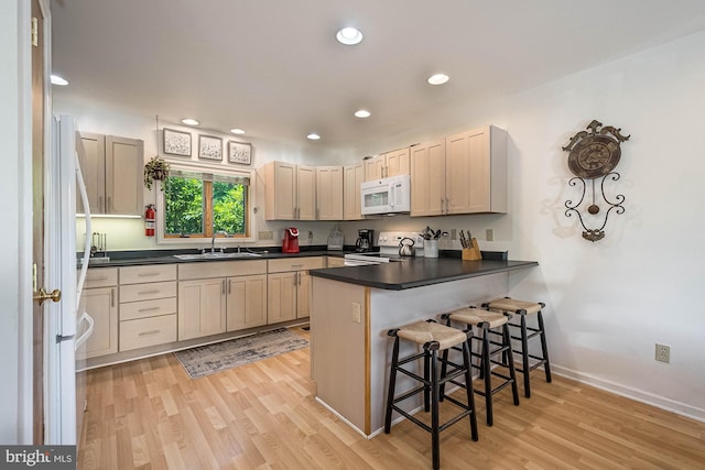 kitchen featuring kitchen peninsula, light wood-type flooring, a breakfast bar, white appliances, and sink