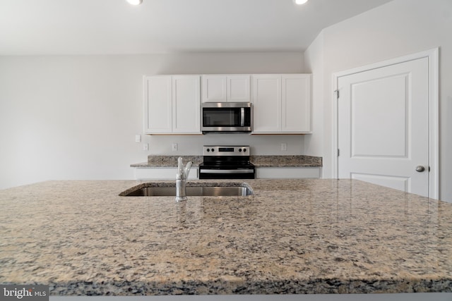 kitchen with light stone counters, stainless steel appliances, white cabinetry, and sink