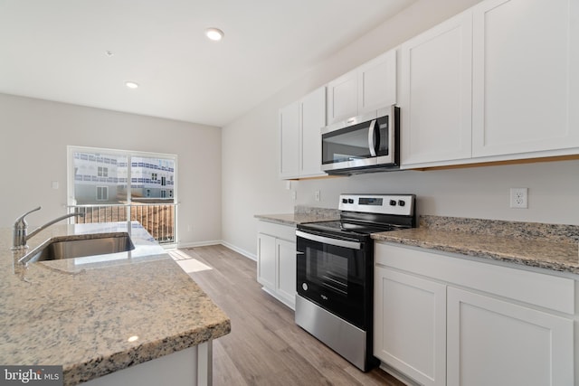 kitchen featuring light stone countertops, stainless steel appliances, sink, light hardwood / wood-style floors, and white cabinetry