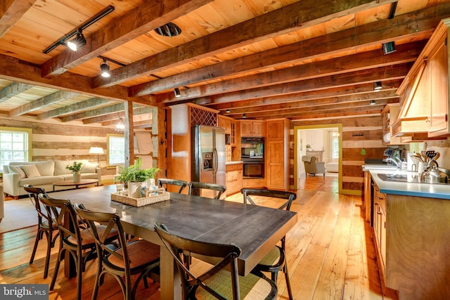 dining room featuring wood walls, a healthy amount of sunlight, light hardwood / wood-style floors, and track lighting