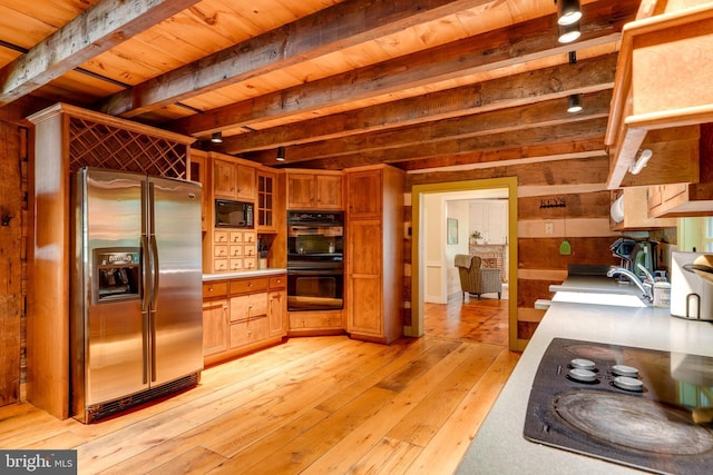 kitchen with sink, beamed ceiling, wood walls, black appliances, and light wood-type flooring