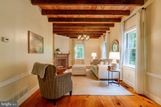 living room featuring beamed ceiling, a notable chandelier, a fireplace, and hardwood / wood-style flooring