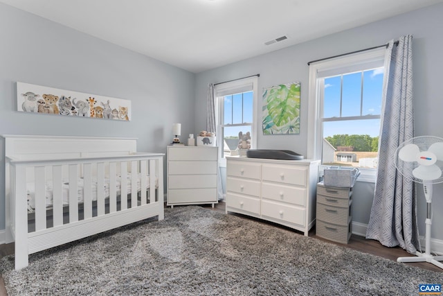 bedroom featuring multiple windows, a crib, and dark wood-type flooring