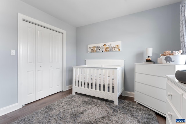 bedroom with a crib, dark wood-type flooring, and a closet