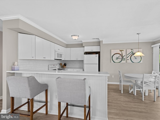 kitchen featuring white cabinetry, kitchen peninsula, white appliances, a breakfast bar area, and decorative backsplash