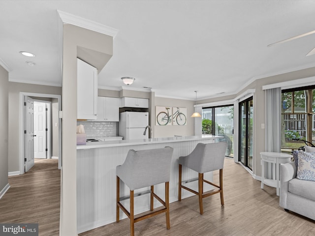 kitchen with backsplash, a kitchen breakfast bar, kitchen peninsula, white fridge, and white cabinetry