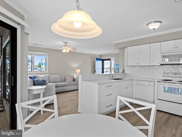 kitchen featuring kitchen peninsula, decorative backsplash, white appliances, sink, and white cabinetry