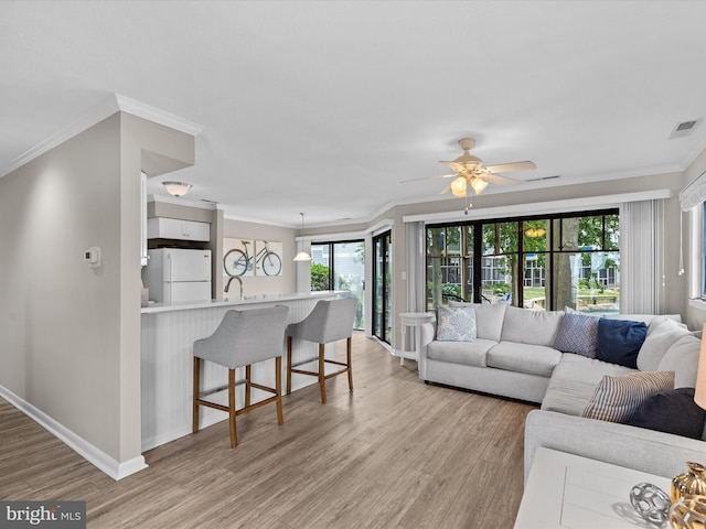 living room featuring ceiling fan, light wood-type flooring, ornamental molding, and a wealth of natural light