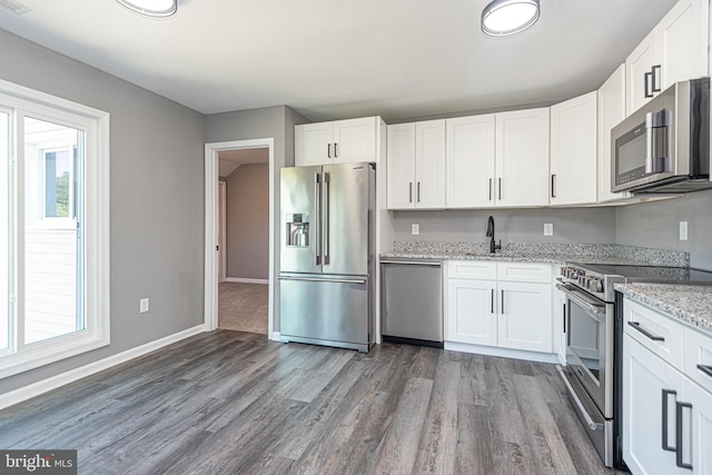 kitchen with white cabinets, stainless steel appliances, light stone countertops, and dark hardwood / wood-style floors