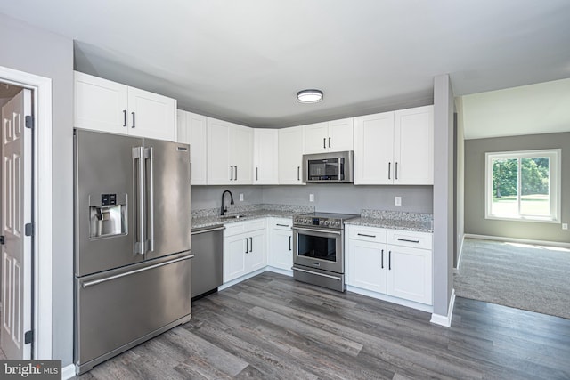 kitchen with light stone countertops, appliances with stainless steel finishes, dark wood-type flooring, sink, and white cabinets