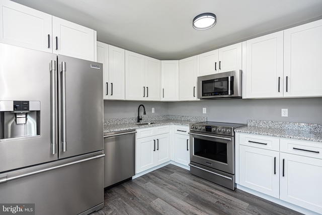 kitchen with white cabinetry, sink, light stone counters, dark hardwood / wood-style floors, and appliances with stainless steel finishes