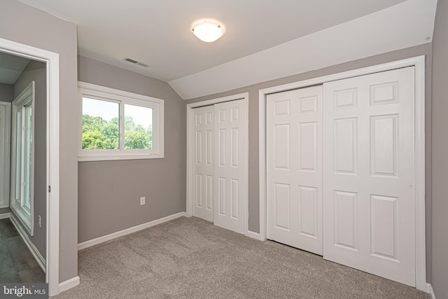 unfurnished bedroom featuring carpet flooring, lofted ceiling, and two closets