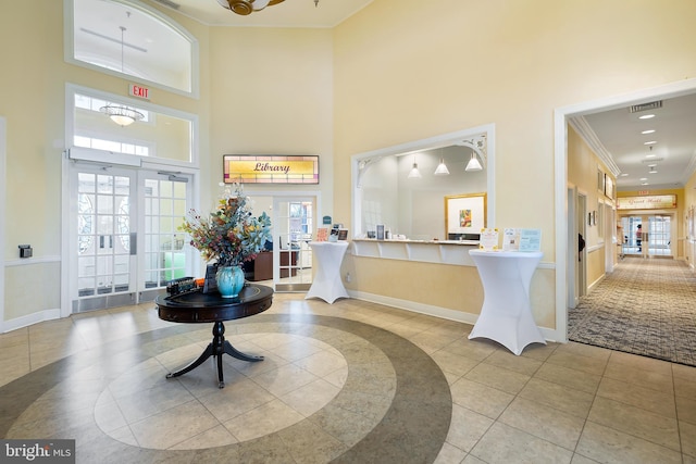 tiled foyer entrance with a wealth of natural light, crown molding, french doors, and a towering ceiling