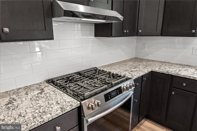 kitchen with decorative backsplash, light stone counters, high end stainless steel range oven, and light wood-type flooring