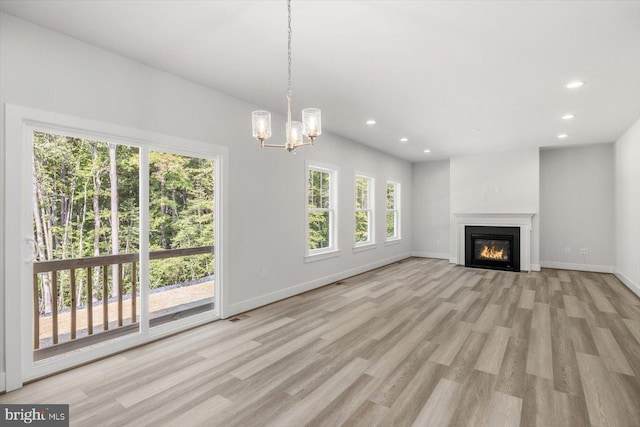 unfurnished living room with plenty of natural light, light hardwood / wood-style floors, and an inviting chandelier