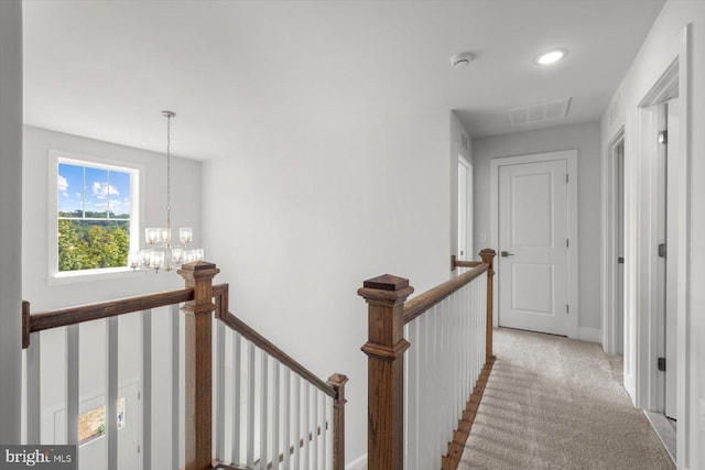 hallway featuring a notable chandelier and light carpet