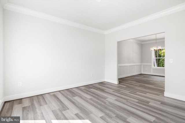 empty room with a notable chandelier, wood-type flooring, and ornamental molding