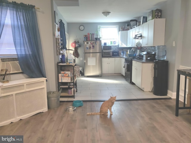 kitchen with decorative backsplash, white cabinets, radiator heating unit, stainless steel refrigerator, and black / electric stove