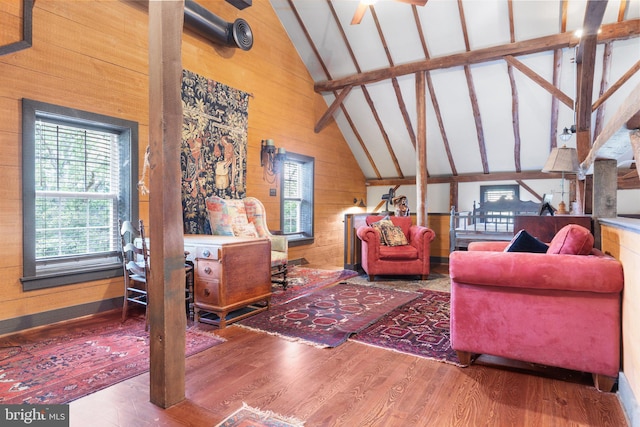 living room with wooden walls, beam ceiling, high vaulted ceiling, ceiling fan, and wood-type flooring