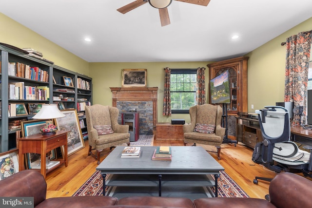 living room with light hardwood / wood-style flooring, a stone fireplace, and ceiling fan