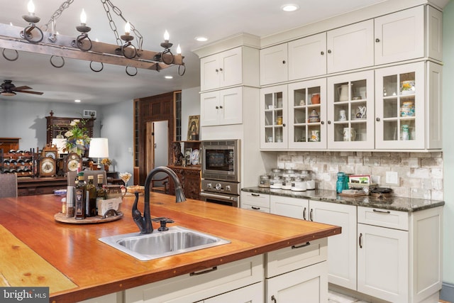 kitchen with wood counters, ceiling fan with notable chandelier, sink, appliances with stainless steel finishes, and backsplash