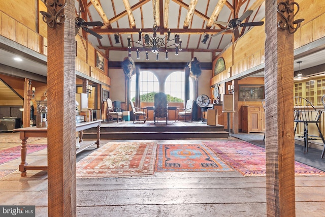 interior space featuring wooden walls, ceiling fan with notable chandelier, high vaulted ceiling, and beam ceiling