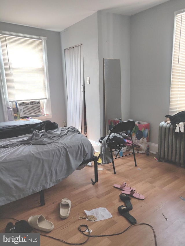 bedroom featuring multiple windows, radiator heating unit, cooling unit, and light wood-type flooring