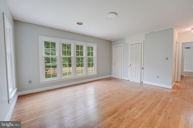 unfurnished bedroom with multiple closets, light wood-type flooring, and multiple windows