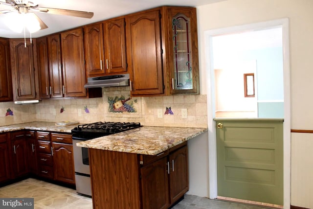 kitchen featuring backsplash, gas range, light stone countertops, and ceiling fan