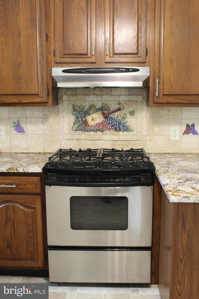 kitchen featuring stainless steel gas range oven, backsplash, and light stone countertops