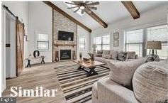 living room featuring a barn door, high vaulted ceiling, light wood-type flooring, beamed ceiling, and a fireplace