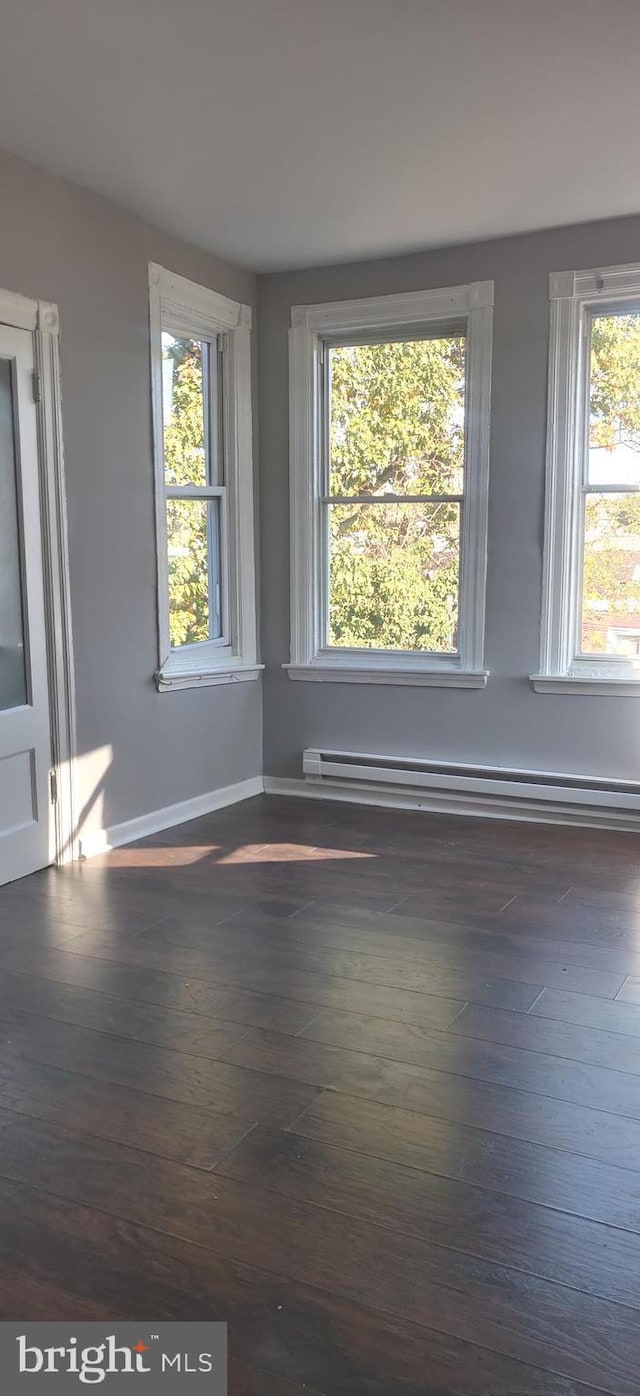 unfurnished room featuring baseboard heating, plenty of natural light, and dark hardwood / wood-style floors