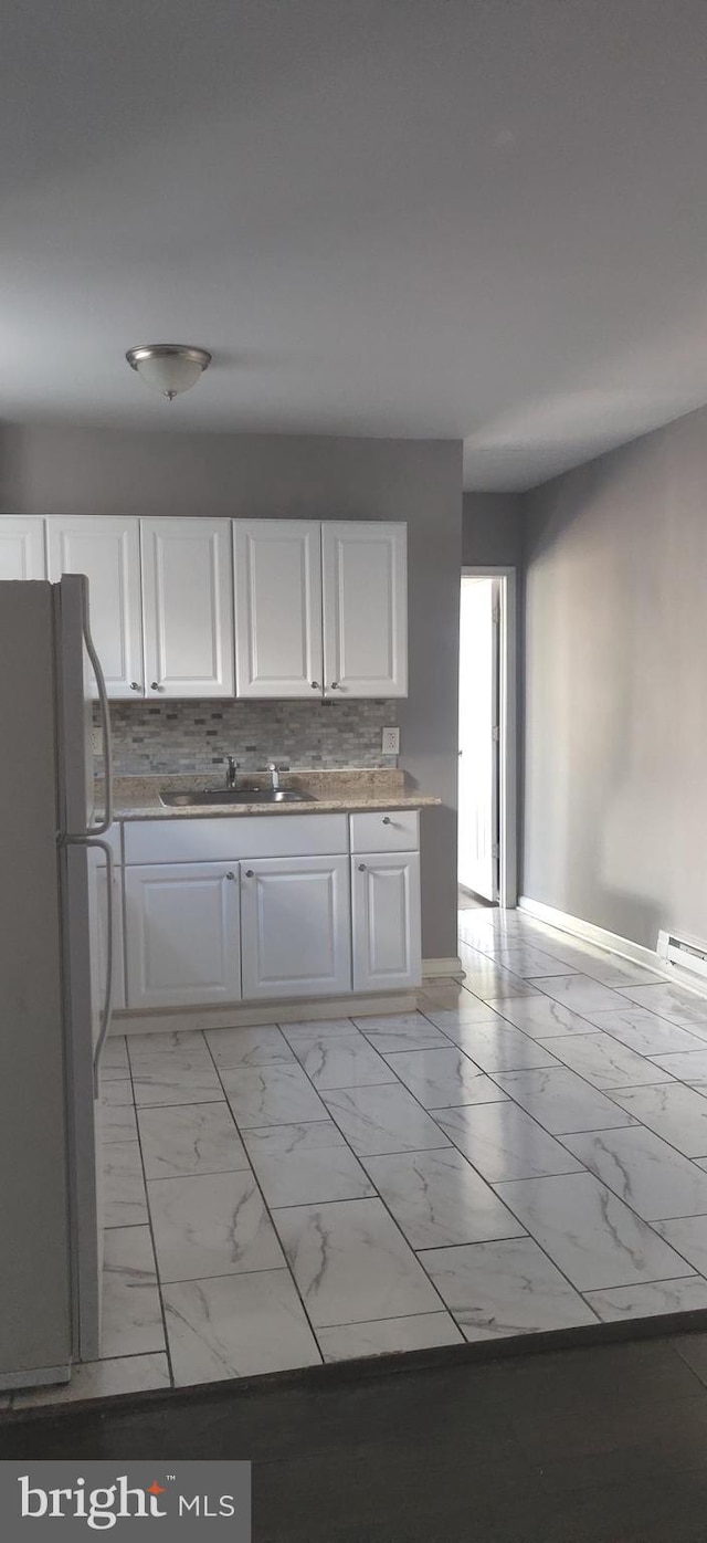 kitchen with tasteful backsplash, fridge, sink, white cabinets, and a baseboard radiator