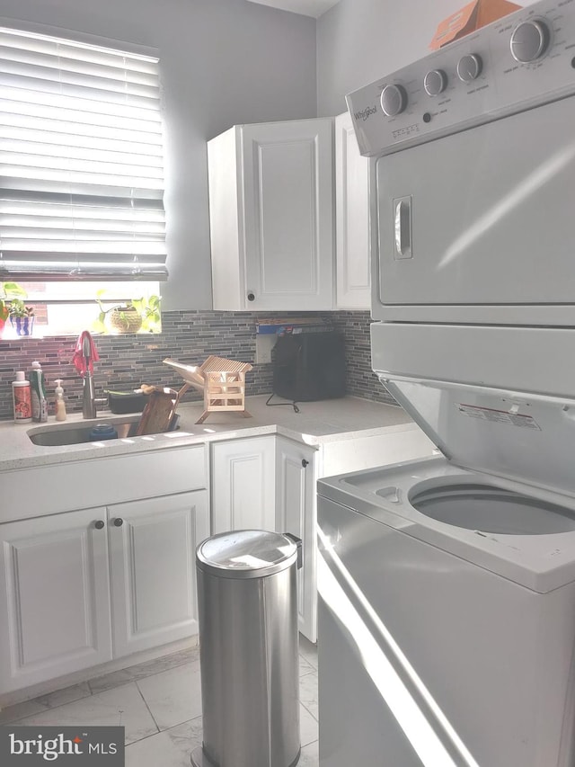 kitchen with tasteful backsplash, white cabinetry, stacked washer and clothes dryer, and sink