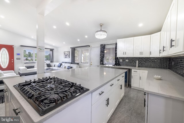 kitchen with light stone countertops, gas stovetop, white cabinets, and vaulted ceiling