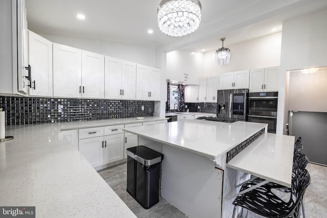 kitchen with multiple ovens, white cabinetry, a notable chandelier, hanging light fixtures, and a center island